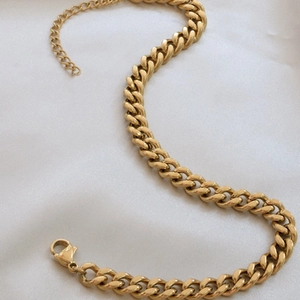 Cavigliera a maglia cubana dorata da donna su elegante sfondo in seta bianca pura