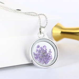 Vista macro di ciondolo rotondo argento con fiori secchi viola e catenina a sfere sottile