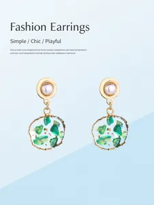 Detail van vintage gouden oorbellen met groene stenen en hangers van hars op blauw