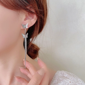 Close-up of elegant silver butterfly earrings with long snake chain tassels on ear