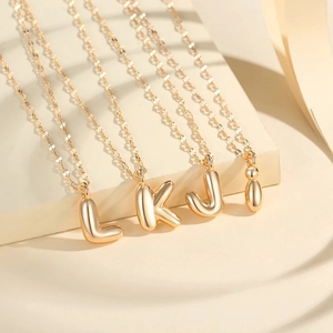 Golden 3D bubble letter necklaces L K J I on minimalist layered display stand