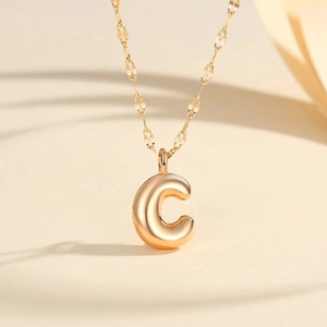 Detail shot of golden bubble letter C pendant with polished mirror finish on a fine chain