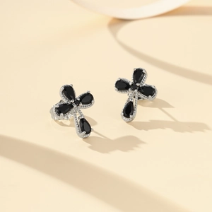 Vista macro de pendientes de cruz plateados con piedras negras en forma de pera y engaste