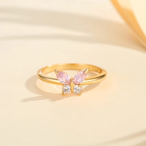 Eleganter goldener Schmetterlingsring mit rosa und klaren Zirkonsteinen auf beigem Grund