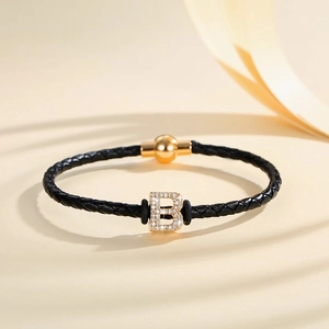 Close-up of black braided leather bracelet with golden diamond-studded B letter pendant