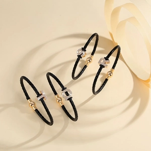 Close-up of black braided leather bracelets with gold metal beads and rhinestone letters