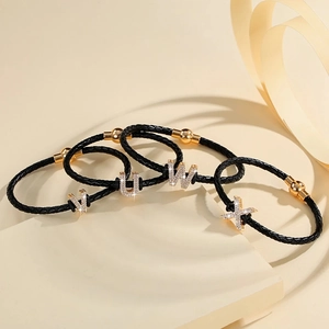Close-up of black braided leather bracelets with gold diamond-set V U W X letter charms