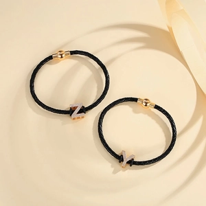 Detail of woven leather bracelets with gold magnetic clasps and zircon letter pendants