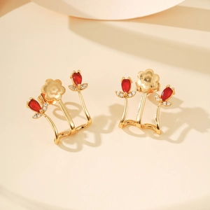 Detail macro-opname van goudkleurige ear cuff met rode peer-zirkonia en bloemrijk accent