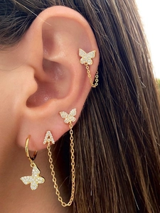 Macro shot of gold butterfly zircon earrings with letter A stud on ear cartilage