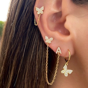 Macro shot of gold butterfly and letter A earring set with zircons on model ear