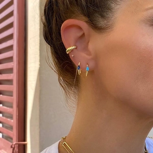 Detail van gouden oorbellen met blauwe zirkoonstenen en geribbelde ear cuff sieraden