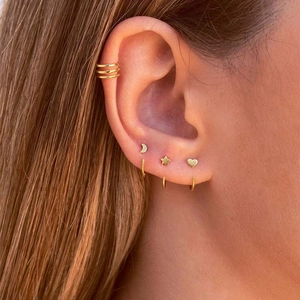 Gros plan de clous d'oreilles cœur, étoile, lune dorés et bague d'oreille sur modèle