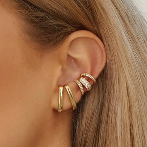 Macro di un set di ear cuff dorati con zirconi incastonati indossati sull'orecchio