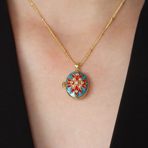 Vintage gouden medaillon ketting met blauwe emaille bloem gedragen door een model