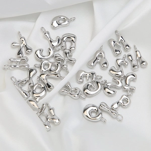 Macro shot of 3D silver bubble alphabet pendants on white silk for DIY jewelry