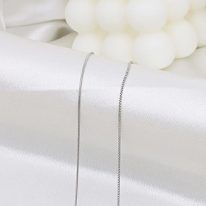 Chaîne serpent et collier box en argent élégamment présentés sur du tissu en soie blanc