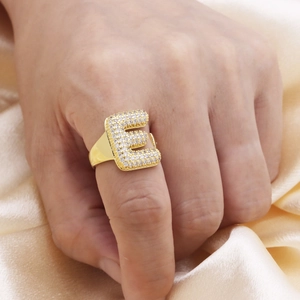 Detailopname van goudkleurige ring met letter E en zirkoon-pavé op champagne satijnen achtergrond