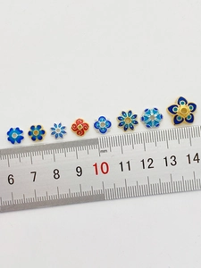 Makro-Detail von 18K vergoldeten Emaille-Blumenperlen neben einem präzisen Messlineal