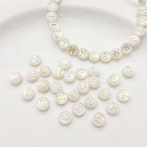 Makro-Detail von Alphabet-Muschelperlen mit Goldbuchstaben für DIY-Armbänder