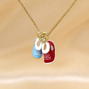 Golden box chain necklace featuring cute blue and red enamel sneaker charms on gold satin background
