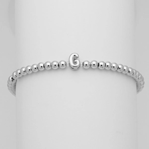 Dettaglio di un bracciale a sfere argentato con un ciondolo a forma di lettera G bombata