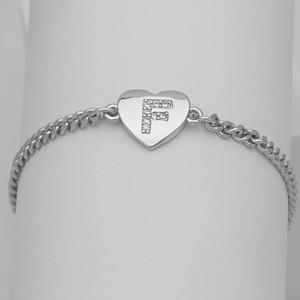 Macro view of silver heart pendant with crystal F initial on cuban link chain