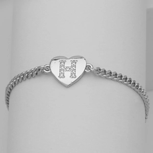 Macro detail of silver heart charm with paved zircon letter H on Cuban link bracelet