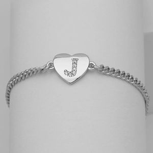 Macro view of silver heart pendant with crystal letter J on flat Cuban link bracelet