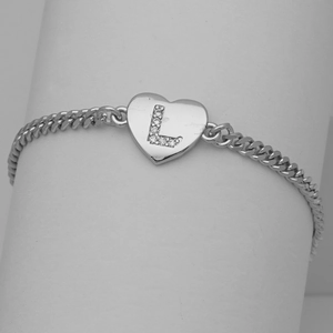 Macro detail of silver heart charm with cubic zirconia letter L on a cuban link chain
