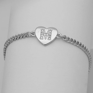 Macro shot of silver heart charm with cubic zirconia letter M on cuban chain bracelet