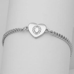 Macro detail of silver heart pendant with letter O and zircon inlay on a curb chain