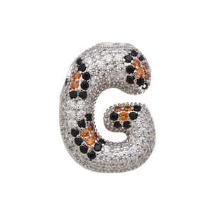 Macro shot of silver letter G pendant featuring micro-paved clear and orange zircons