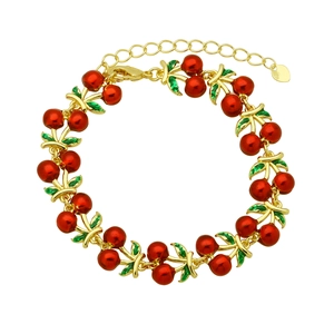 Golden chain bracelet with red cherry pendants and green enamel leaves on white background