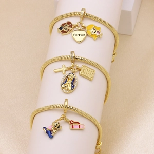 Three gold snake chain bracelets with enamel charms and crystal cross on white velvet stand