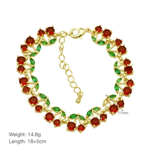 Detail view of gold cherry bracelet with red crystal fruits and green leaf charms