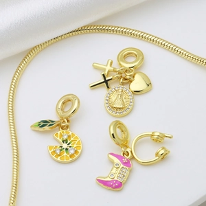 Gold snake chain bracelet with religious cross, lemon slice, and pink game controller charms