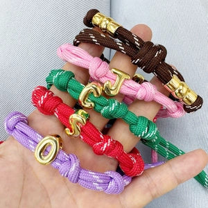 Colorful woven rope bracelet featuring golden bubble alphabet charms on denim background