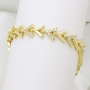Dettaglio di un bracciale placcato oro 18K con maglie a V e zirconi su supporto bianco