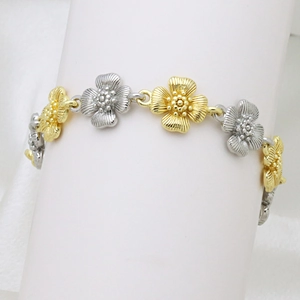 Detailed close-up of two-tone gold and silver flower link bracelet on a white display stand