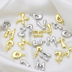 Makroaufnahme von Alphabet-Anhängern im Bubble-Stil auf weißer Seide für DIY-Schmuck
