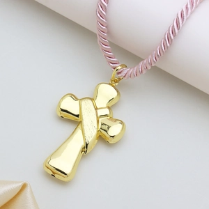 Close-up of polished gold-plated cross pendant with a pink braided cord necklace