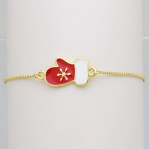 Macro shot of gold Christmas glove bracelet with red enamel and snowflake charm