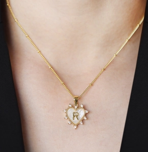 Detail of a golden heart pendant with mother of pearl shell and crystal pavé on letter R