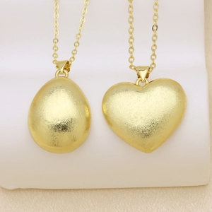 Detalle de colgantes de corazón y óvalo con acabado cepillado en oro de 18K y cadena