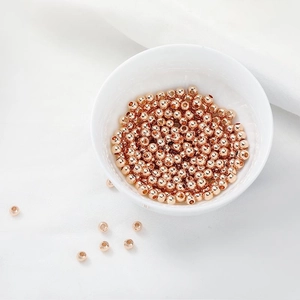 Macro detail of rose gold-plated round spacer beads in a white bowl for DIY jewelry making