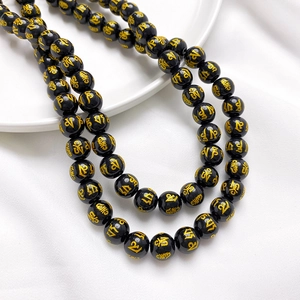 Close-up of black glass beads with gold Mantra engraving on a white ceramic dish