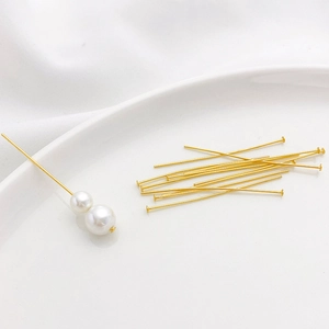 Golden T-pins for DIY jewelry making with white pearls on a white ceramic plate