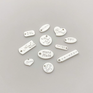 Detalle de colgantes plateados para joyas DIY con grabados de Handmade y Love