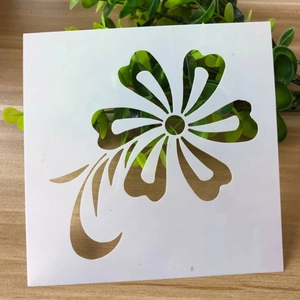 Close-up of white plastic square stencil with hollow floral and swirling line patterns